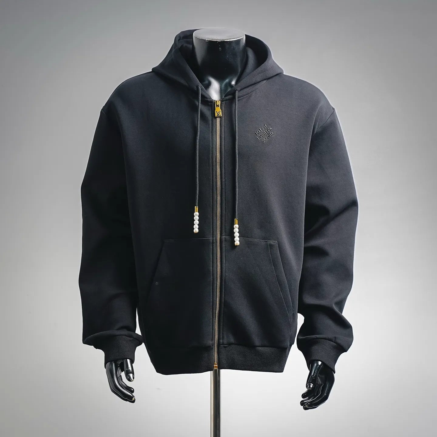 Black zip-up hoodie with hood, front pockets, gold zipper, pearl drawstring pulls