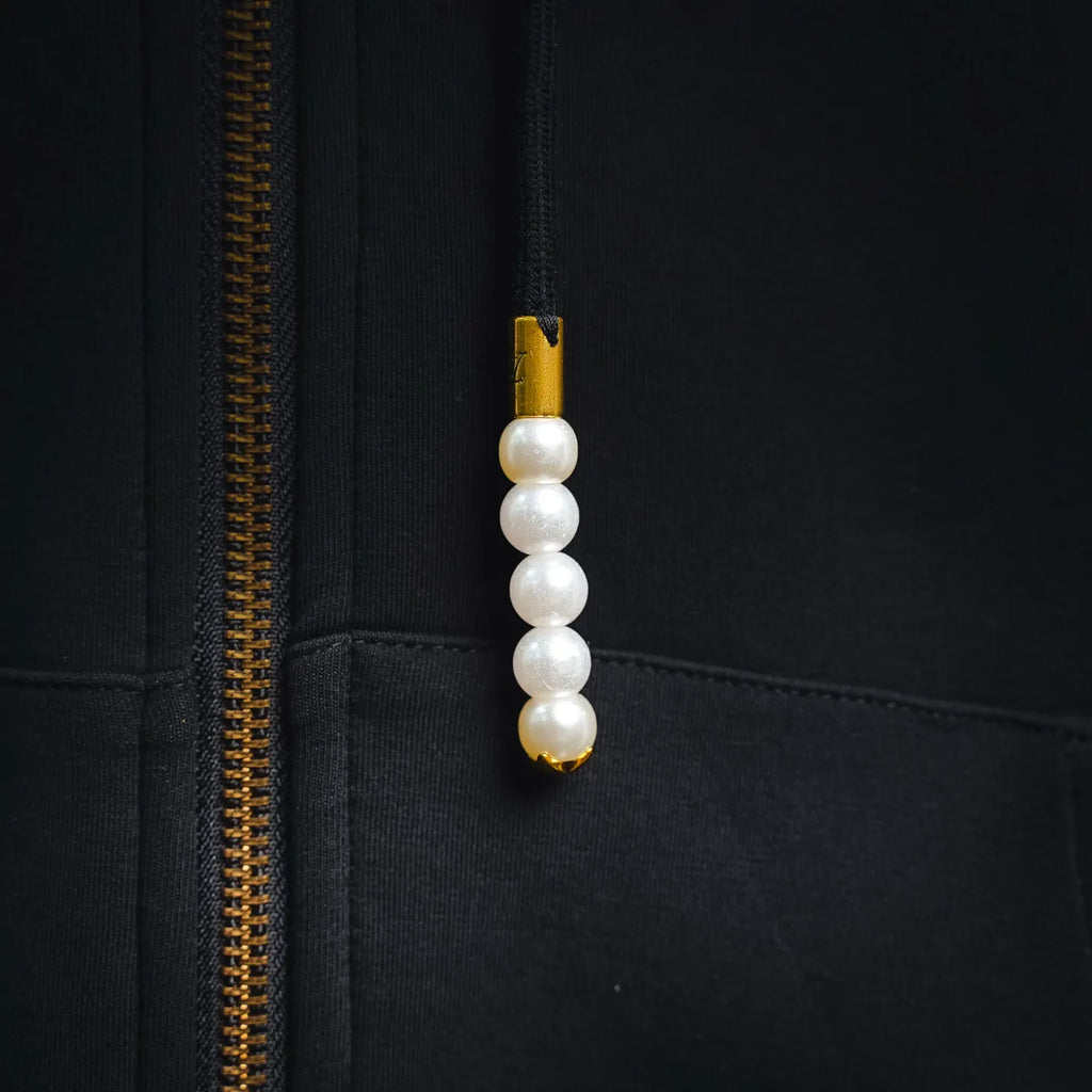Black hoodie zipper close-up with gold teeth and pearl pull charm