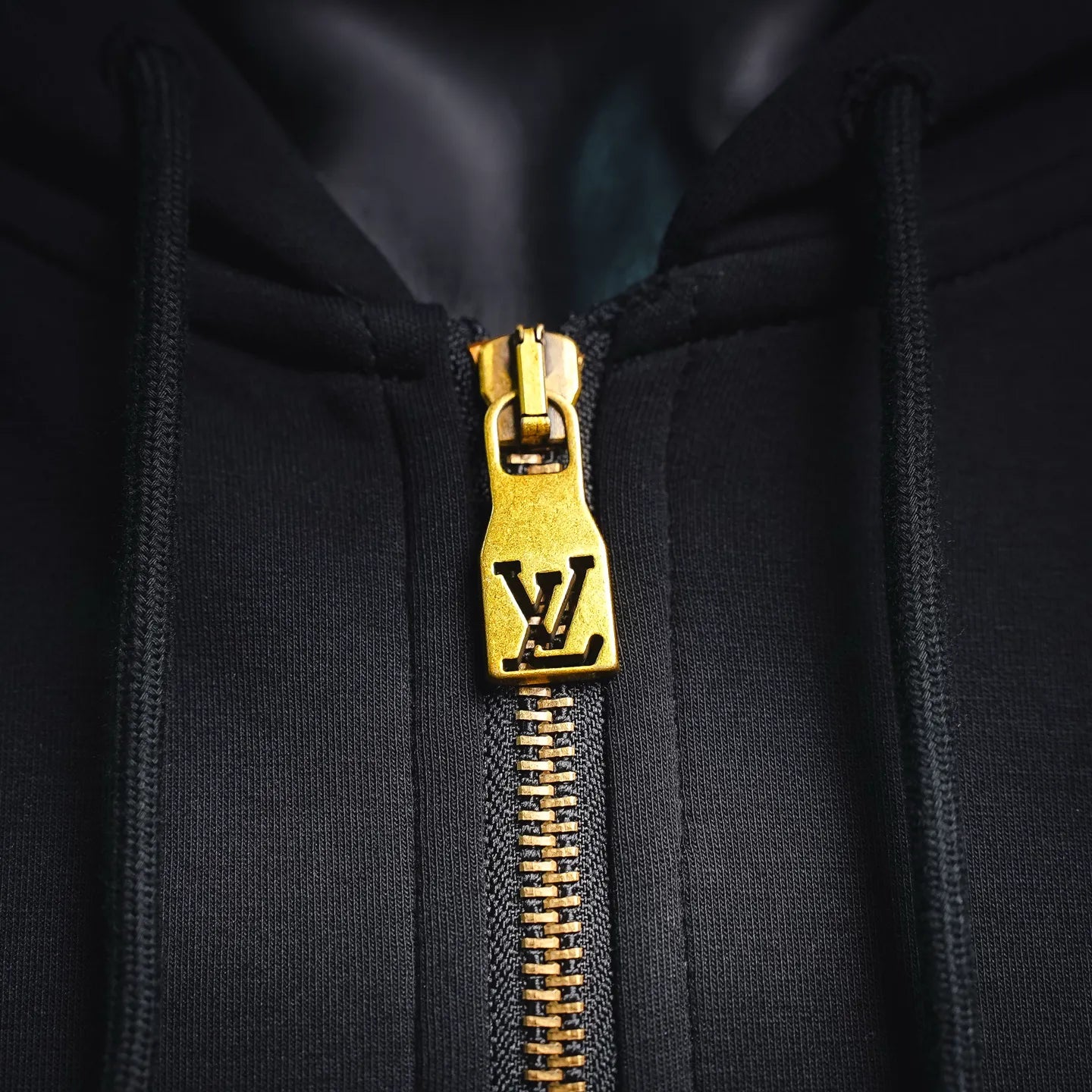 Gold zipper pull with LV emblem on black hoodie