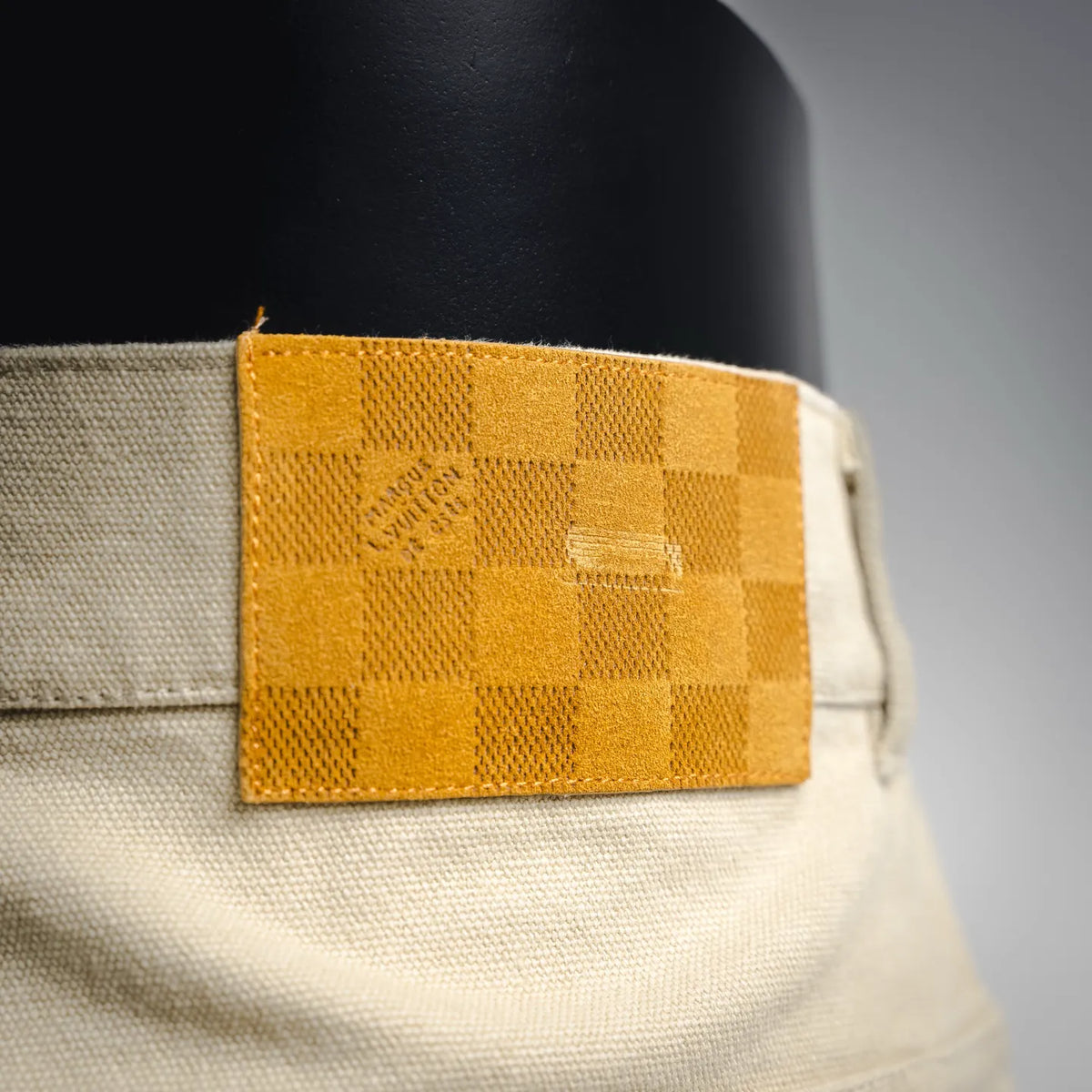 Light beige pants with yellow check logo patch at waistband