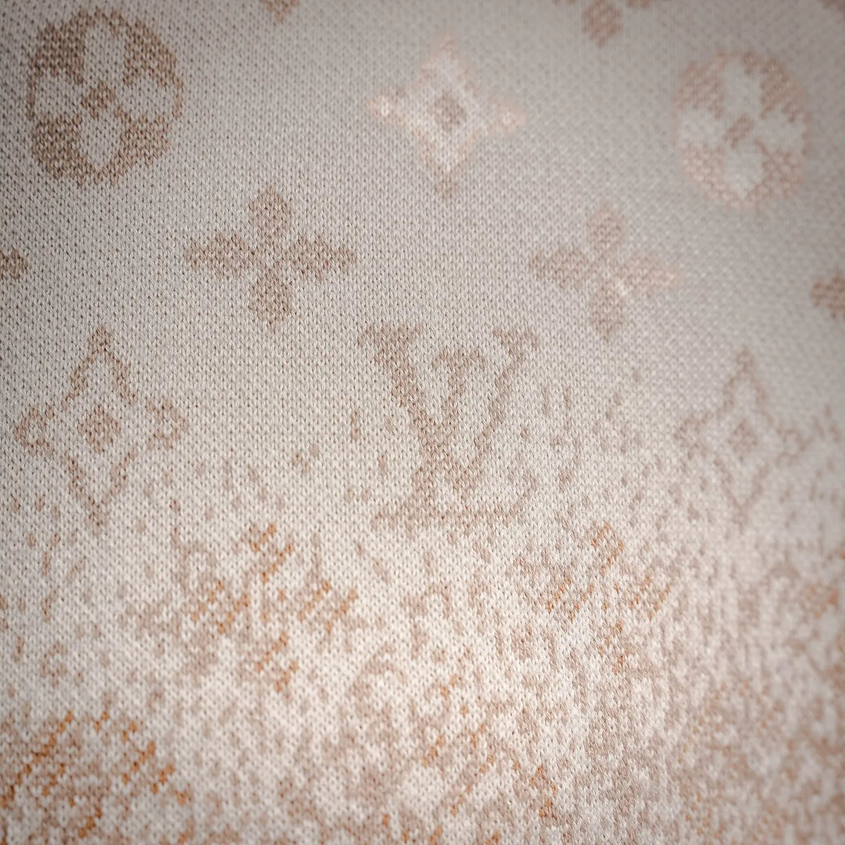 Close-up of cream knit fabric with scattered LV monogram motifs.