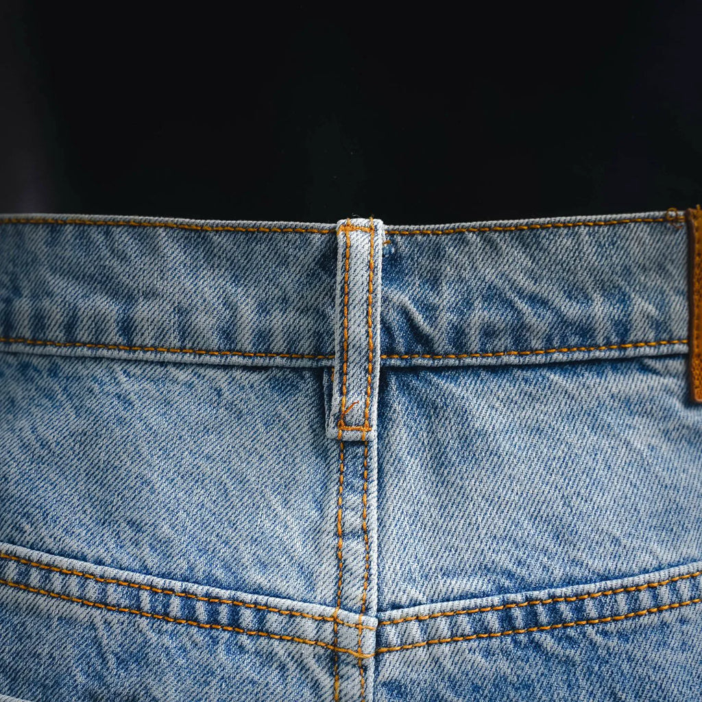 Light blue denim waistband with orange topstitching and reinforced center seam