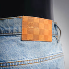 Orange-brown leather belt patch on light blue denim waistband with stitching