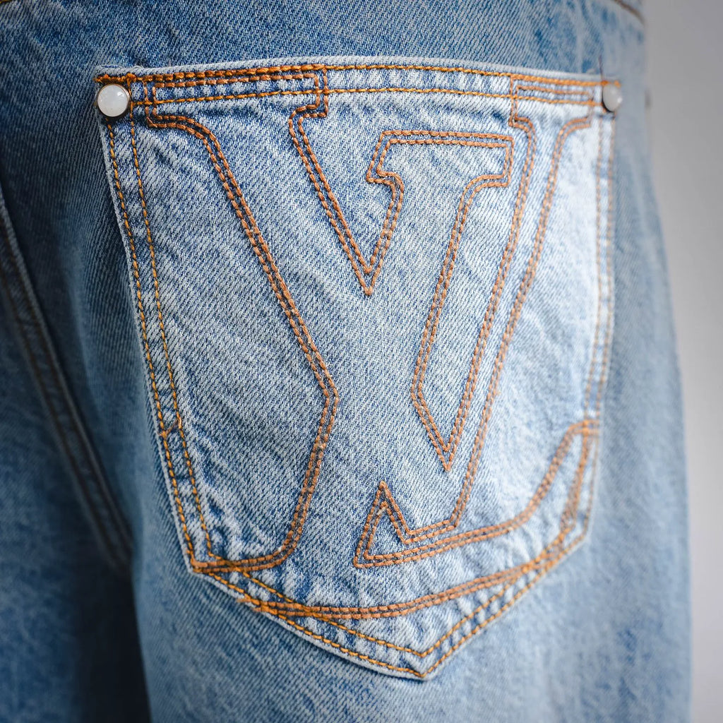 Light blue denim back pocket with orange LV-style embroidery and double-row stitching