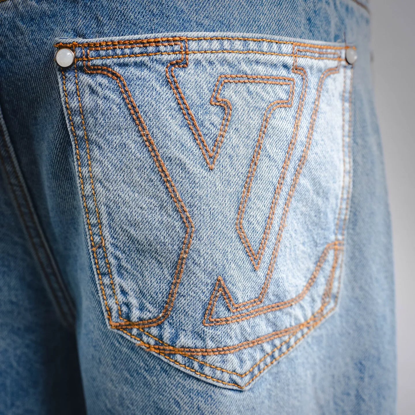 Light blue denim back pocket with orange LV-style embroidery and double-row stitching