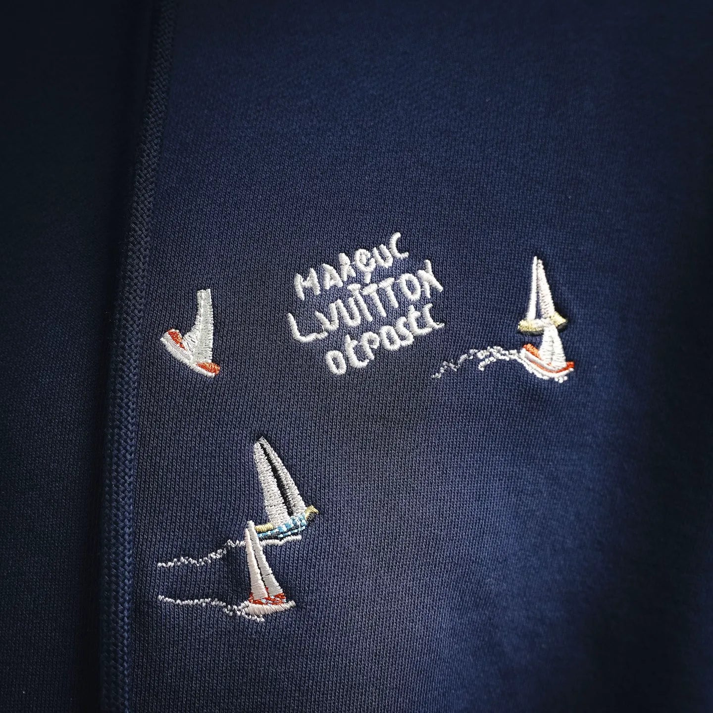 Navy hoodie with embroidered text and small sailboat motifs