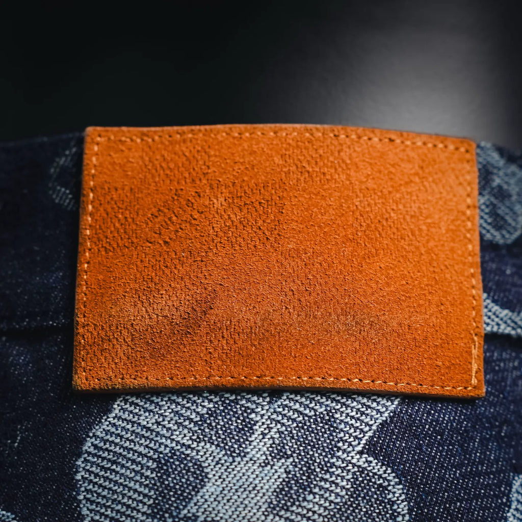Orange leather-like label with stitched edges on dark denim pants