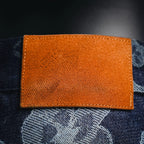Orange leather-like label with stitched edges on dark denim pants