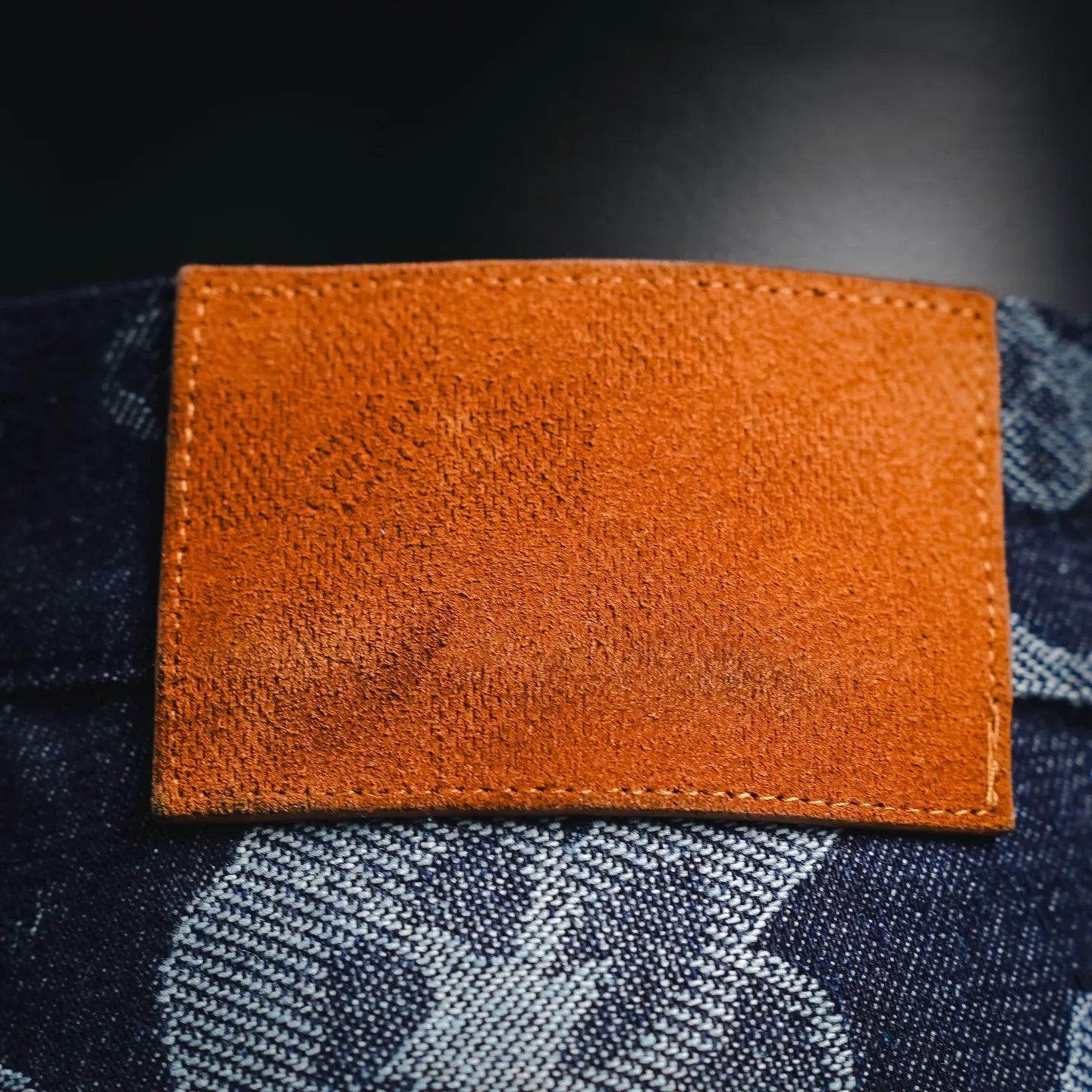 Orange leather-like label with stitched edges on dark denim pants