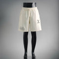 Cream elastic-waist shorts with drawstring, side pockets, and small logo print