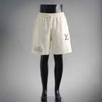 Cream elastic-waist shorts with drawstring, side pockets, and small logo print