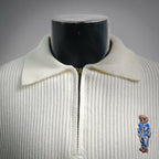 Off-white knit polo with point collar, half-zip front, and bear logo on chest