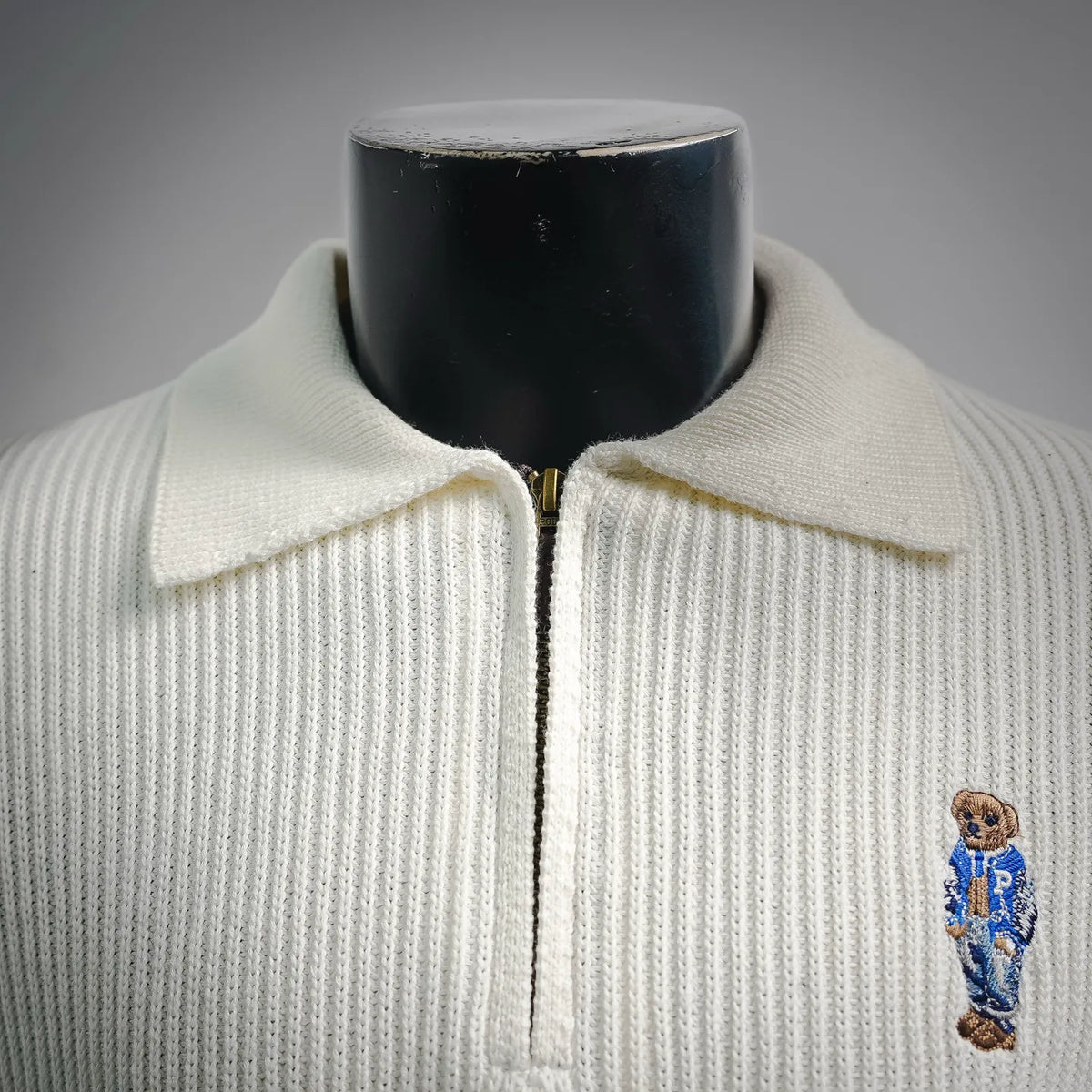 Off-white knit polo with point collar, half-zip front, and bear logo on chest