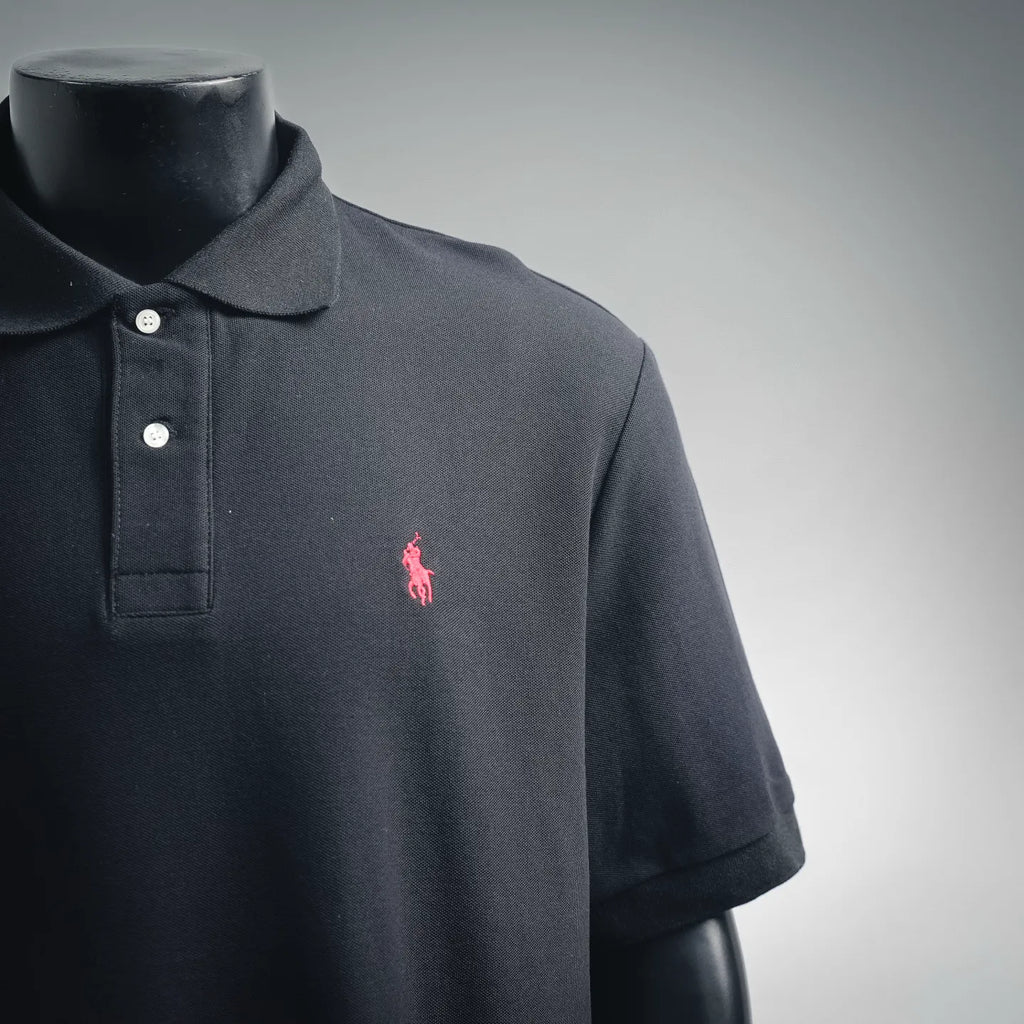 Dark navy polo shirt front close-up with collar buttons and pink embroidered logo