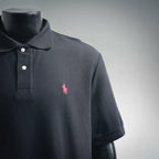 Dark navy polo shirt front close-up with collar buttons and pink embroidered logo