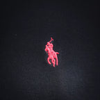 Pink embroidered polo player logo on dark navy polo shirt fabric