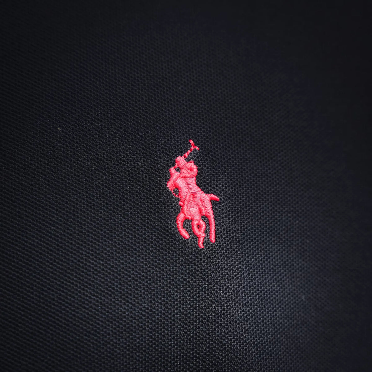 Pink embroidered polo player logo on dark navy polo shirt fabric