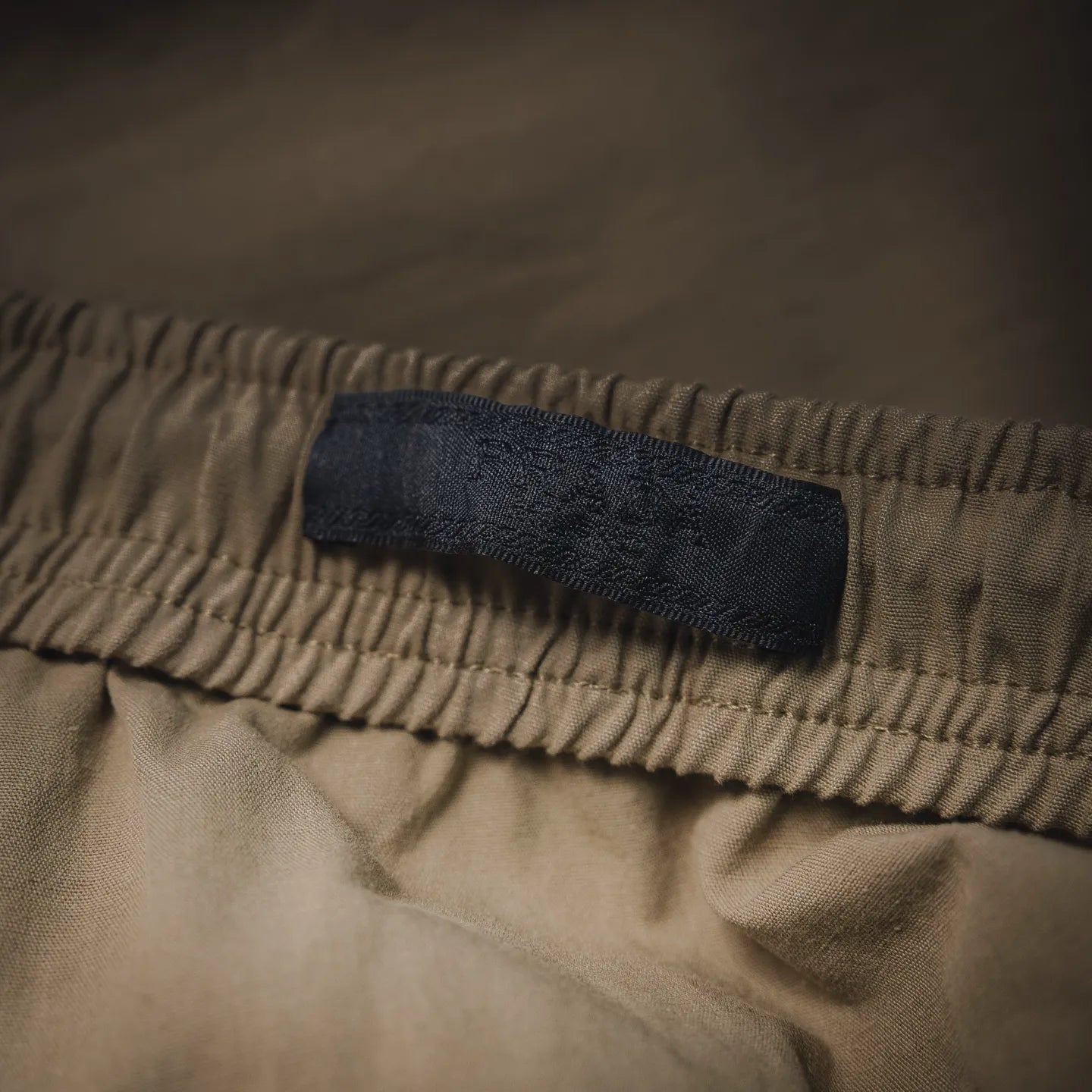 Beige pants with dark fabric logo label on elastic waistband