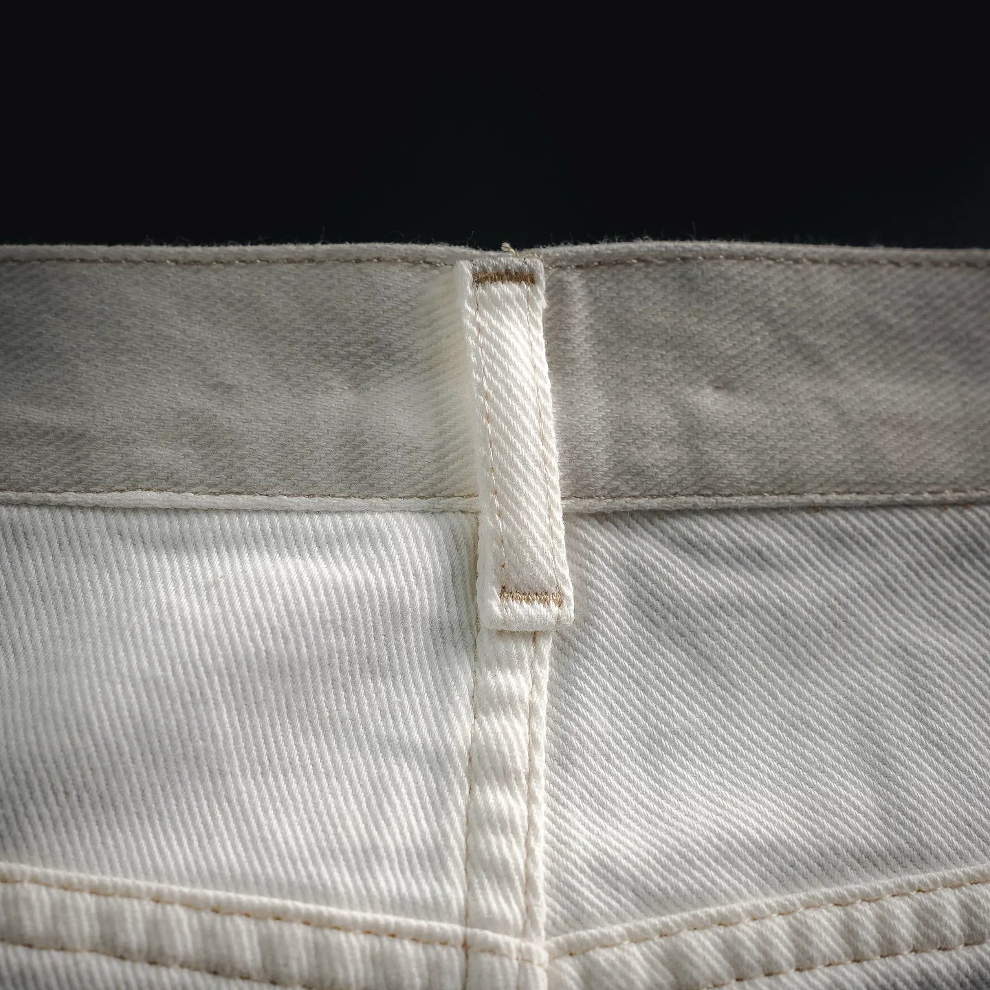 White pants waistband seam with inner label and visible stitched panel.