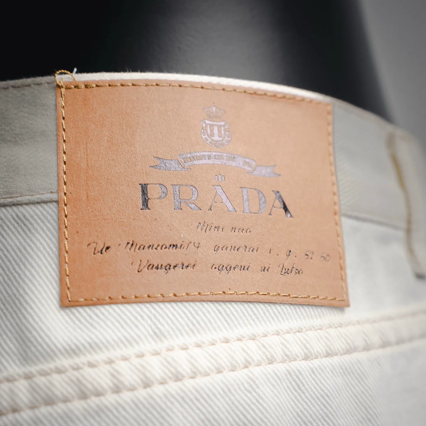 Prada logo leather label on the waistband of white pants.