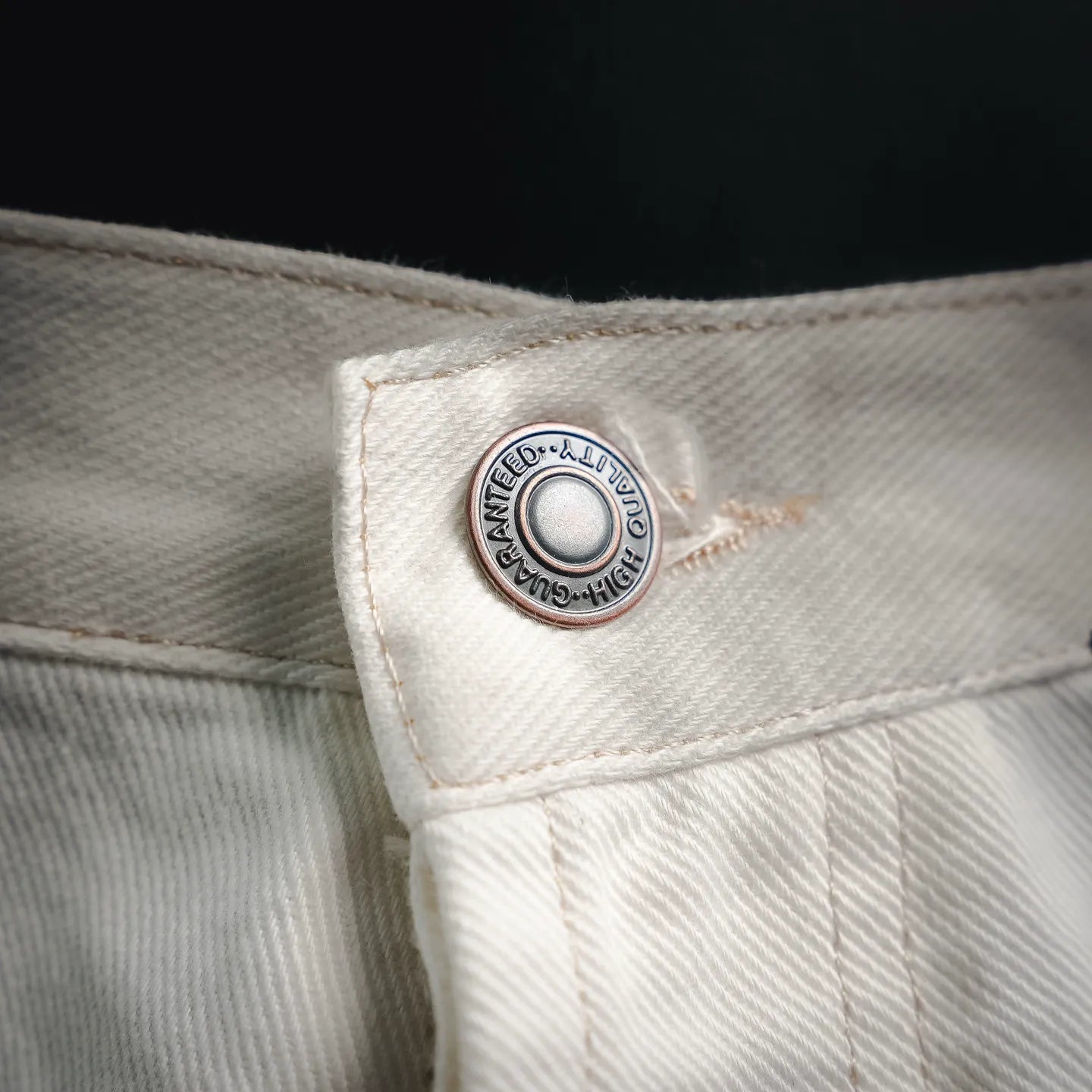 Round logo patch on white pants waistband with leather trim.