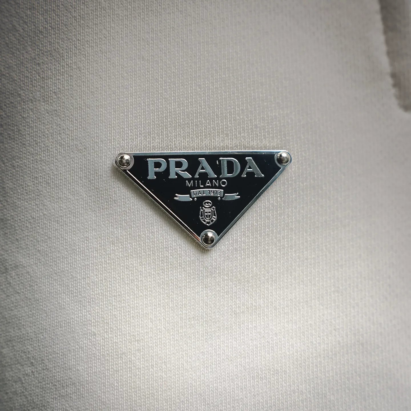 Prada Milano triangular logo patch on white fabric