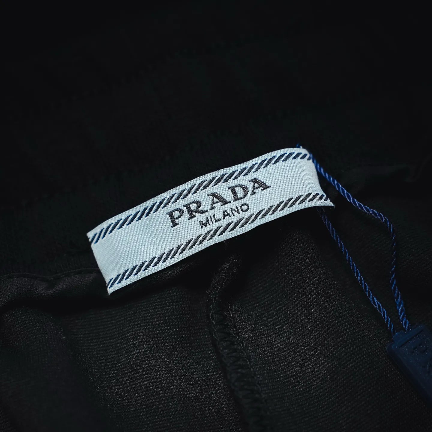 Prada label tag with blue stitched trim on black shorts