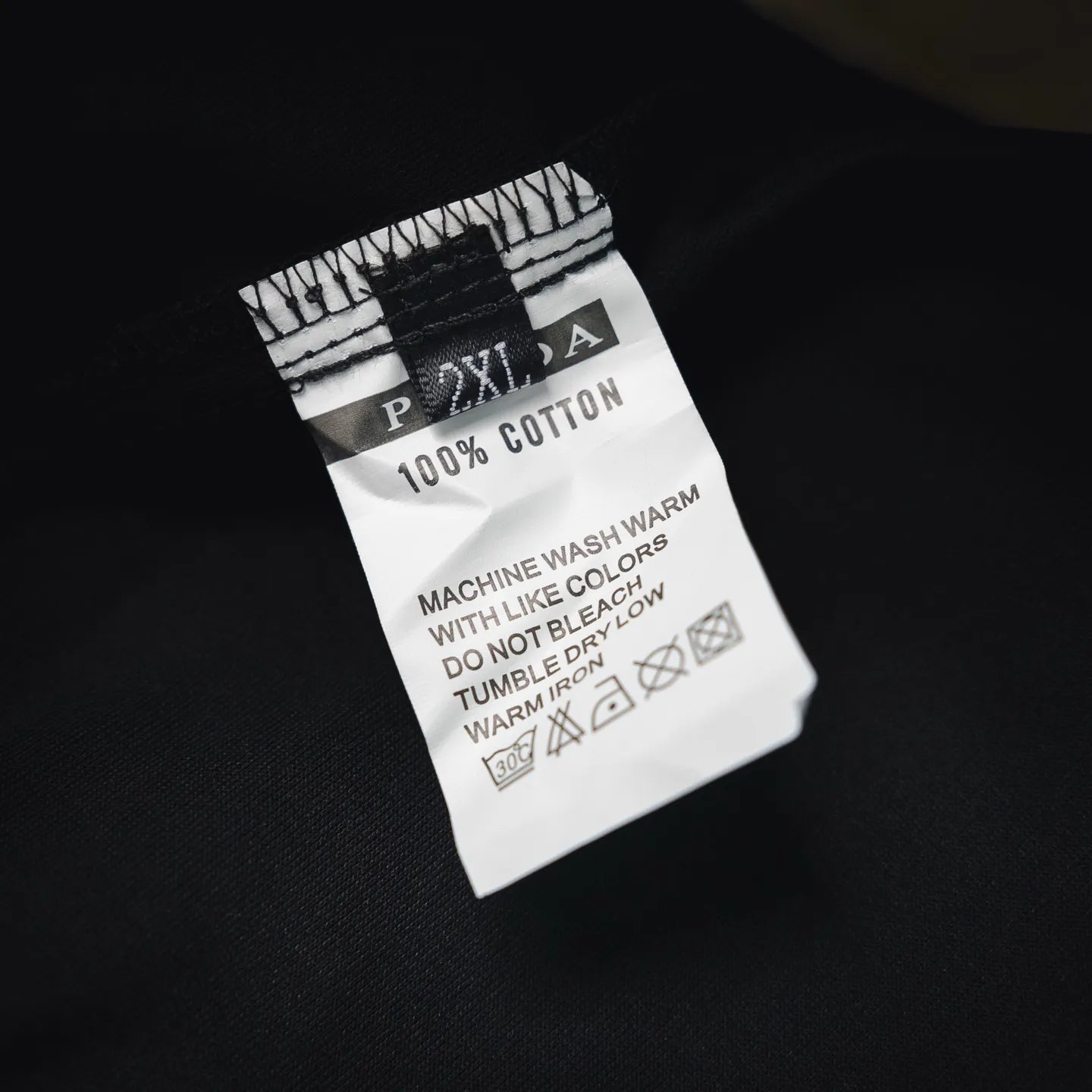 Black pants care label showing 100% cotton and machine wash warm