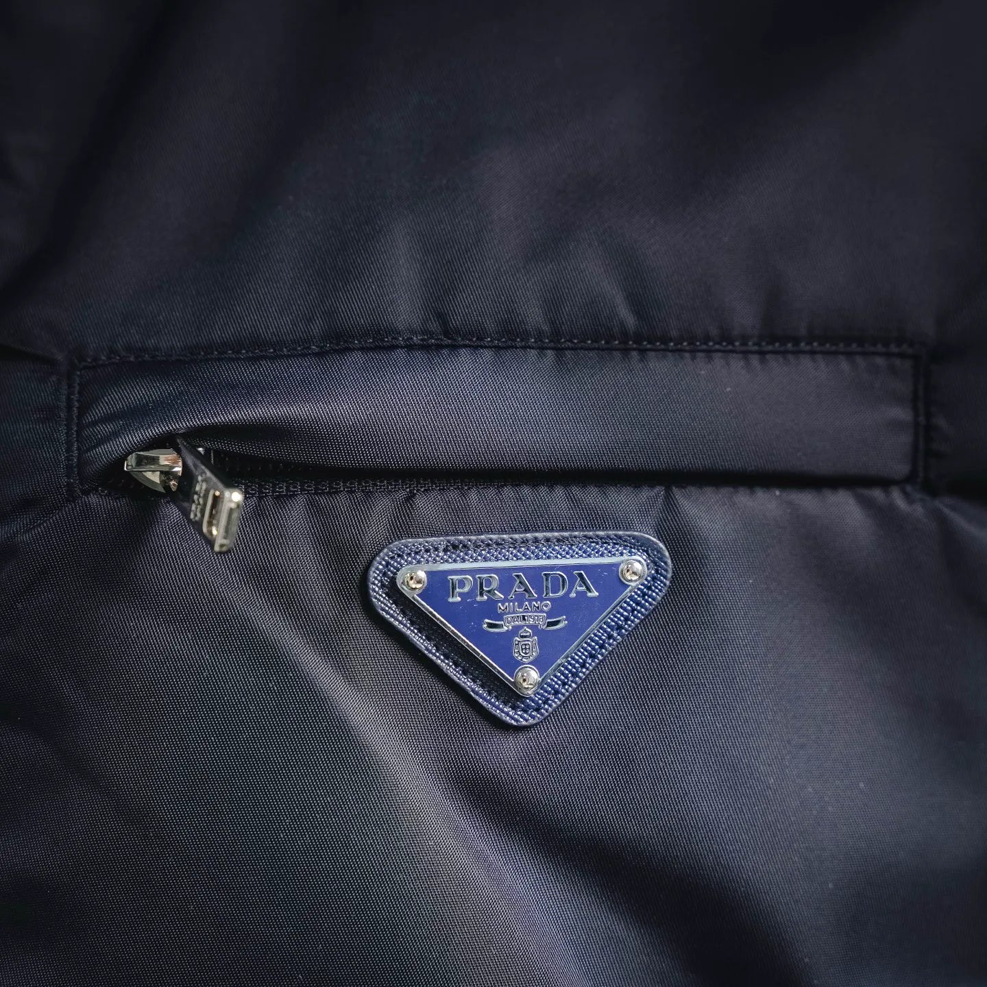 Prada triangular logo patch on navy jacket placket near zipper
