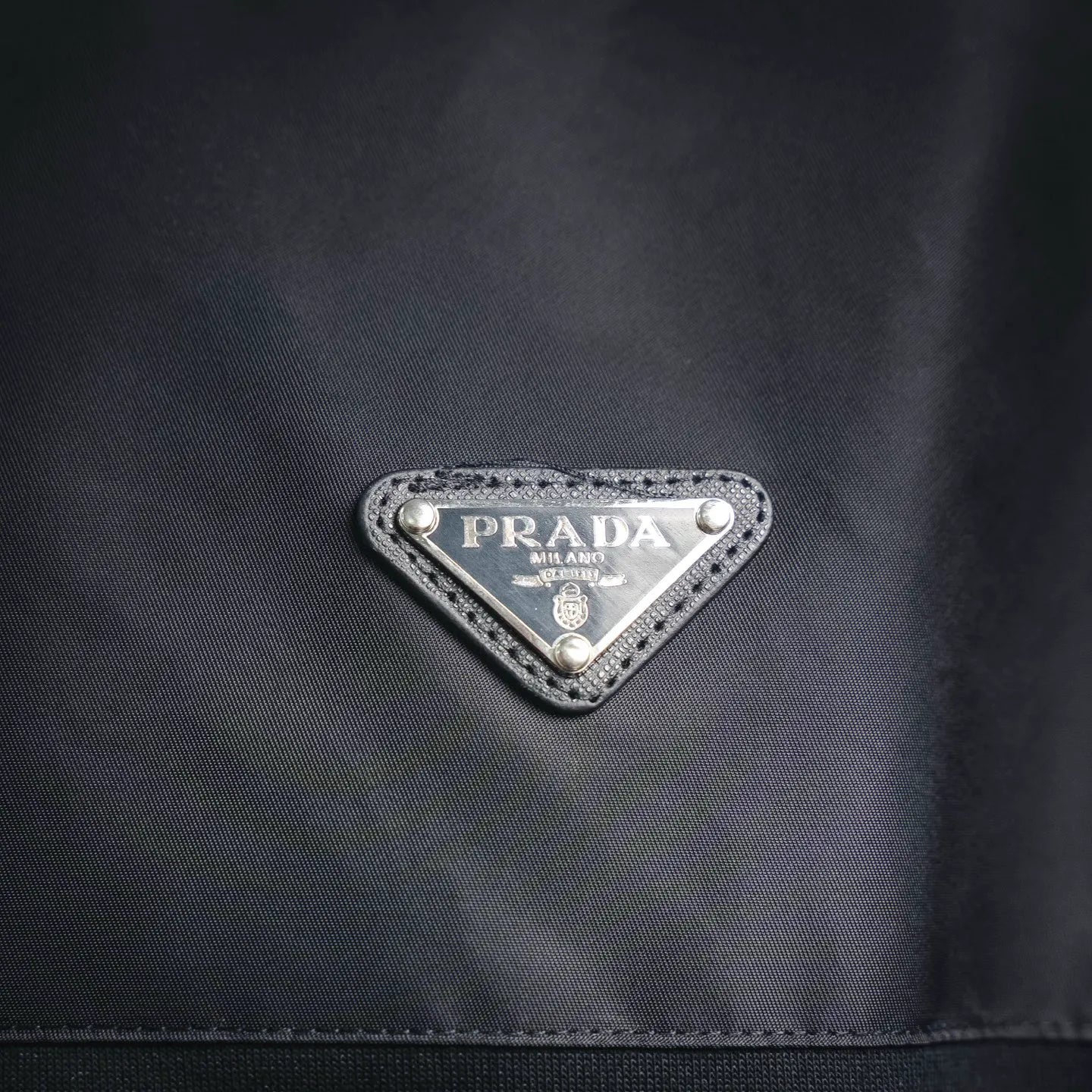 Prada triangular logo badge on dark jacket chest