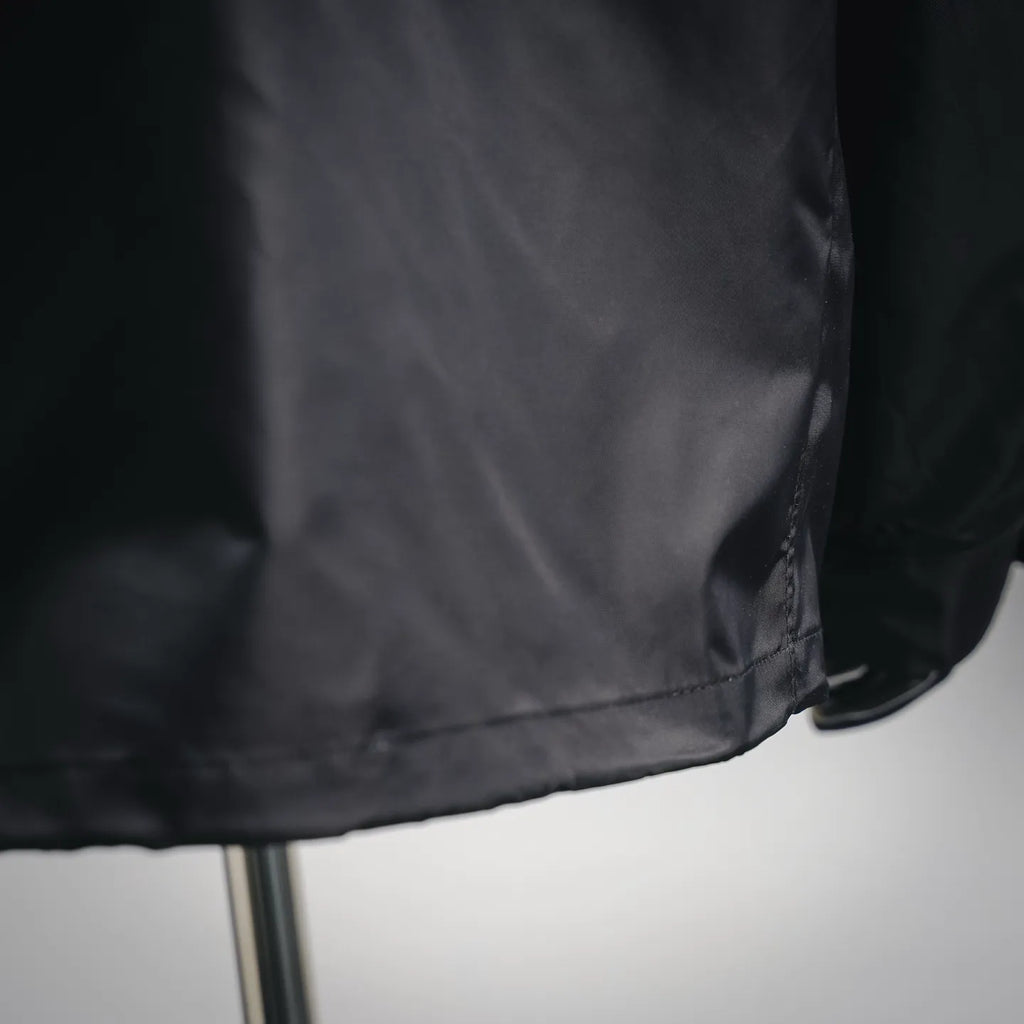 Black jacket bottom hem close-up with stitched seam and slight fabric gathering