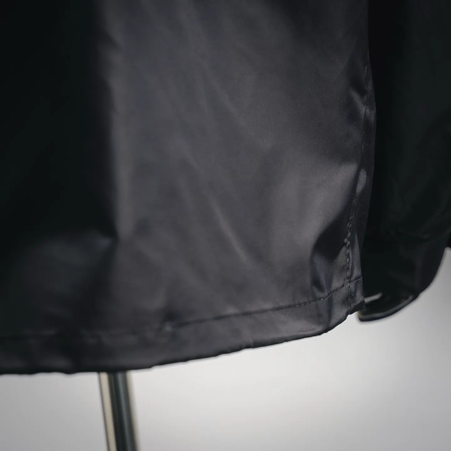 Black jacket bottom hem close-up with stitched seam and slight fabric gathering