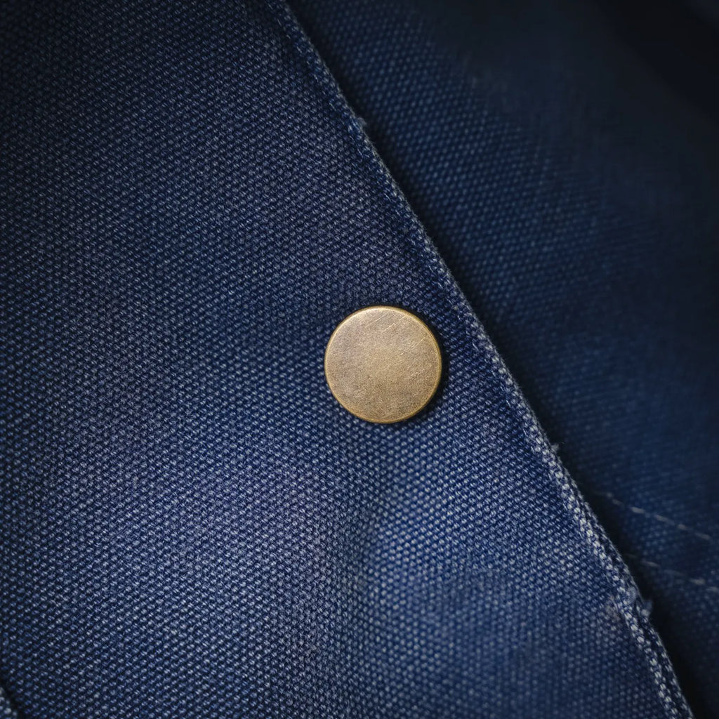 Round brass-style snap button on light blue denim jacket