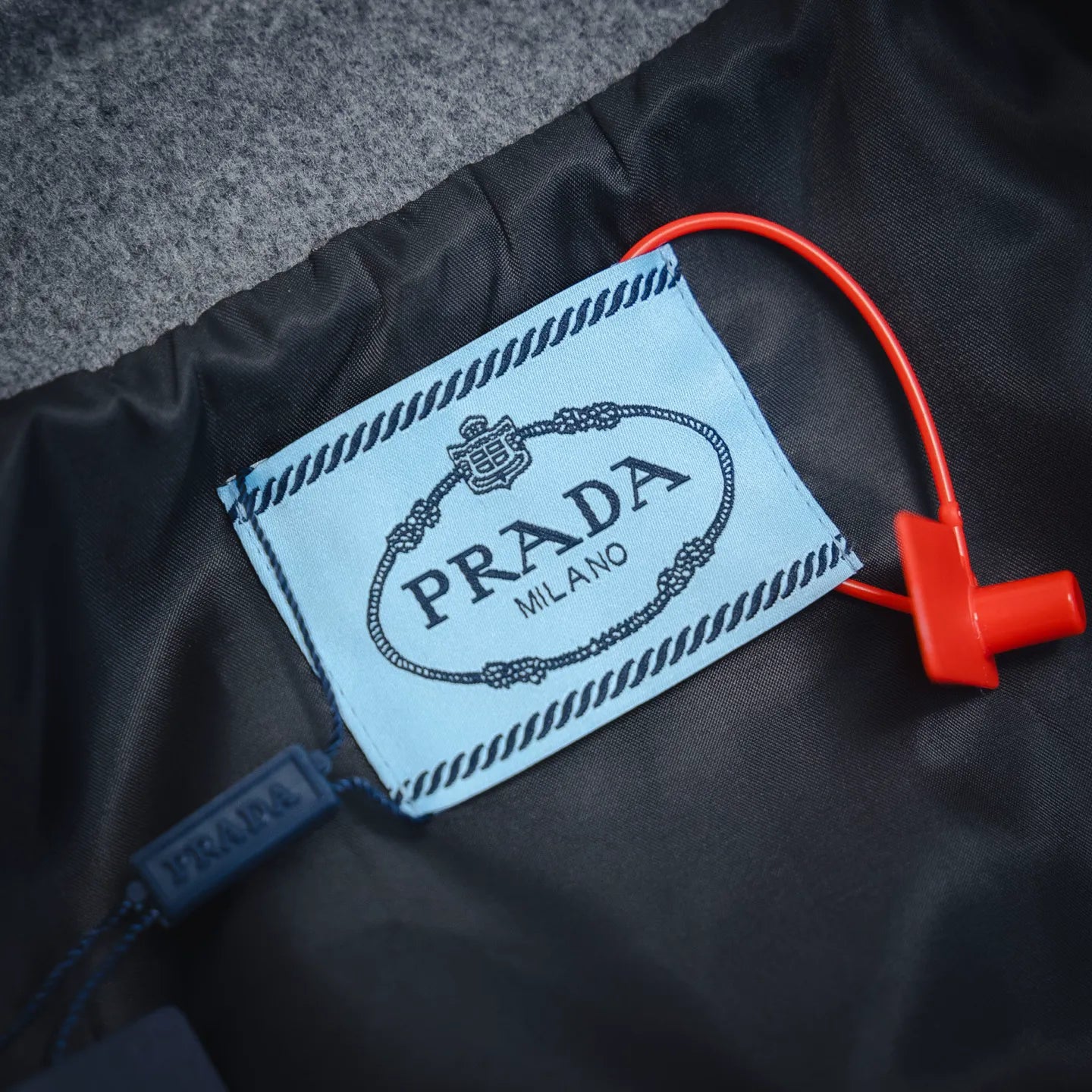 Prada Milano fabric label on dark lining with red plastic tag