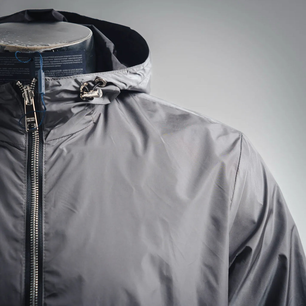 Front upper view of dark gray hooded jacket with zipper and metal hardware at hood