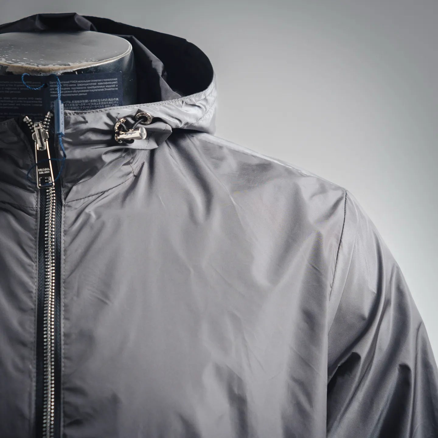 Front upper view of dark gray hooded jacket with zipper and metal hardware at hood