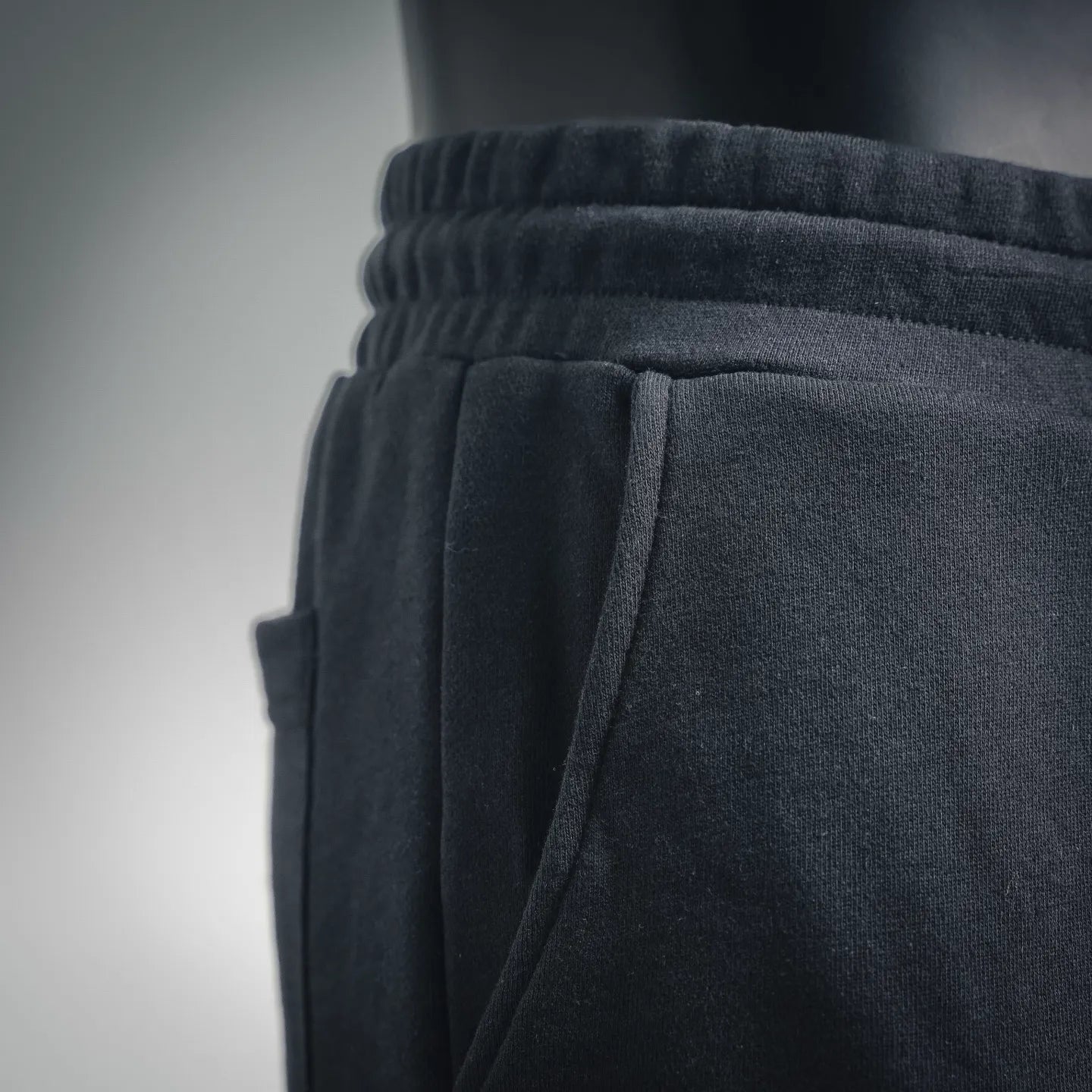 Elastic waistband and side view of dark shorts with pleated front