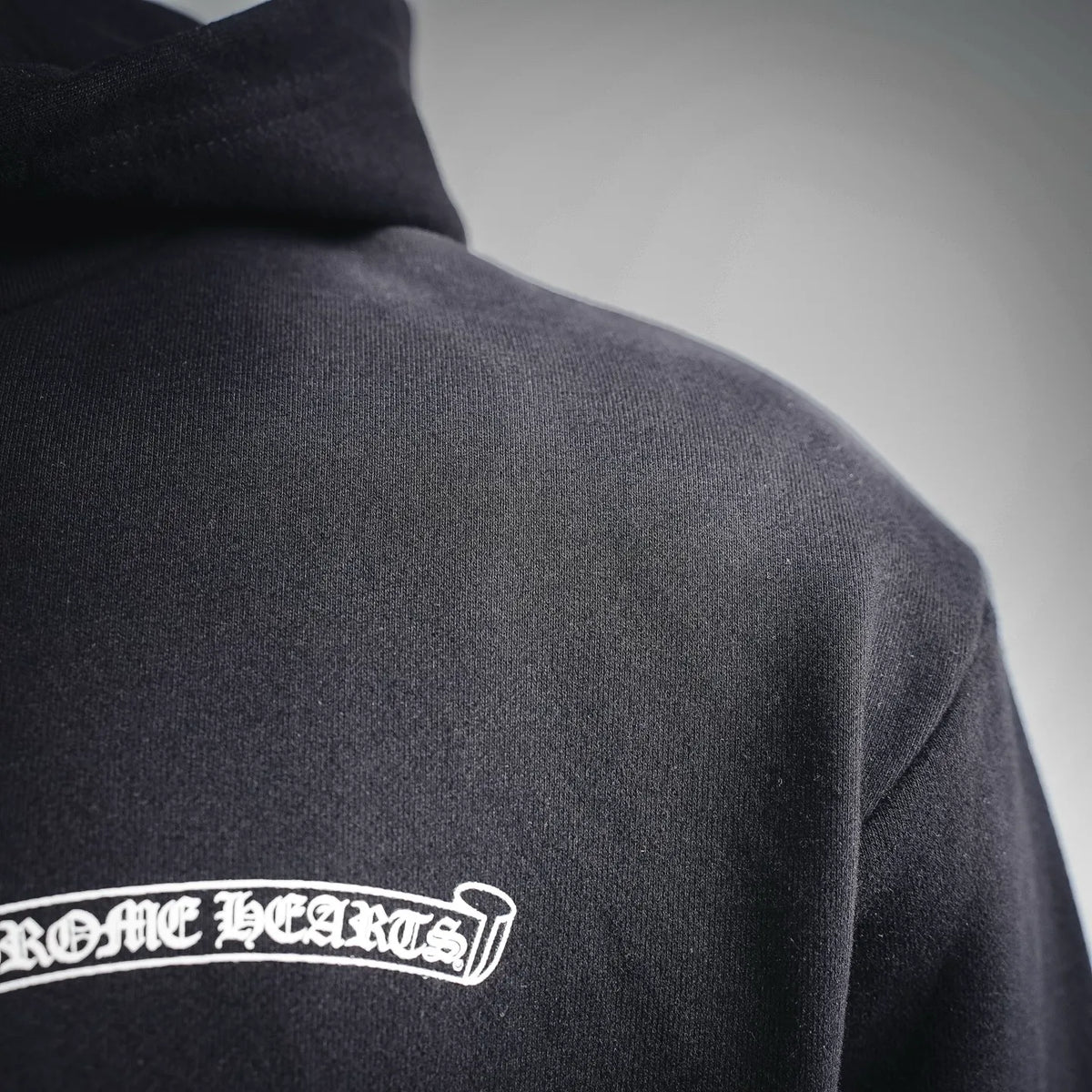 Black hoodie back hem area with 'CHROME HEARTS' logo print near shoulder.