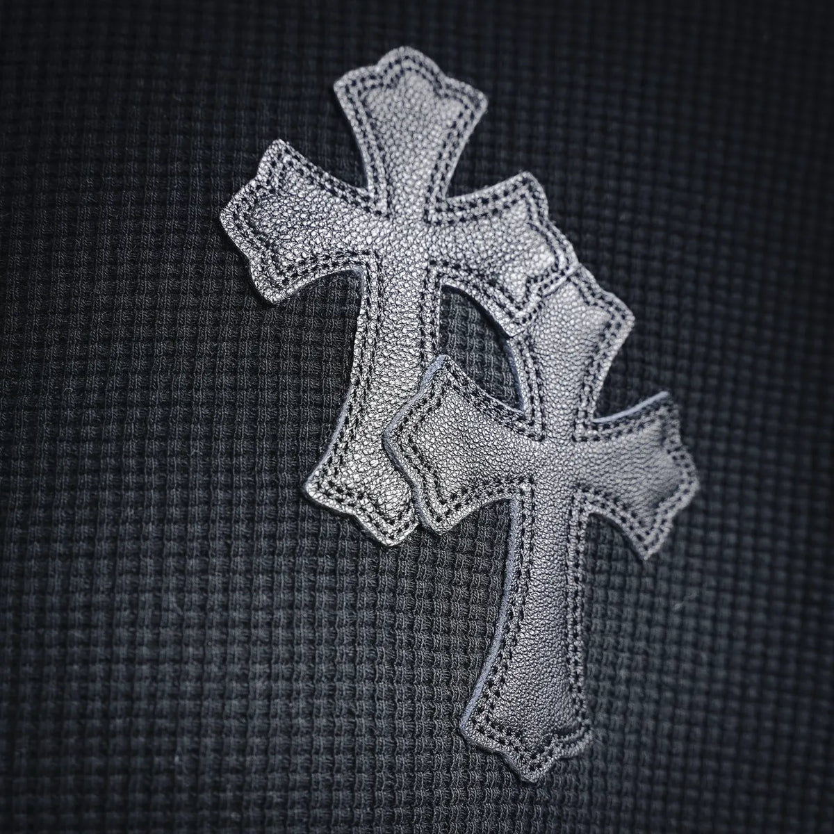 Embroidered silver cross motif on the chest of a dark long-sleeve henley