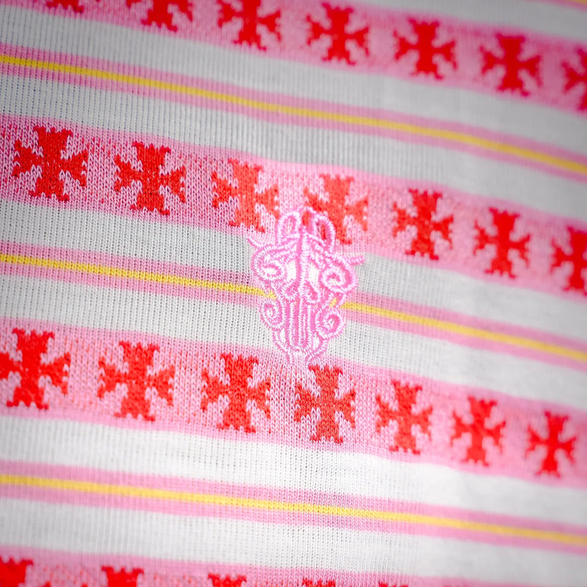 Close-up of polo chest panel, ornate red motif embroidery between stripe bands