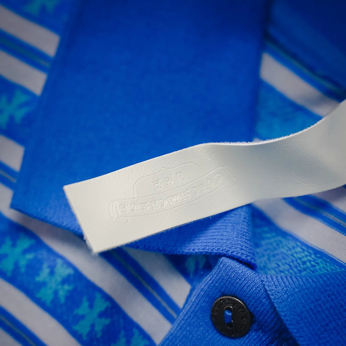 Collar hem detail with fabric tag and button on blue and white striped polo