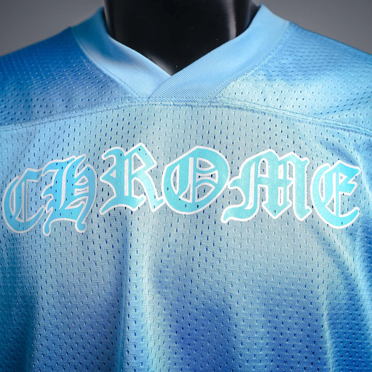 Light blue V-neck jersey close-up with arched front logo text and stitched seam