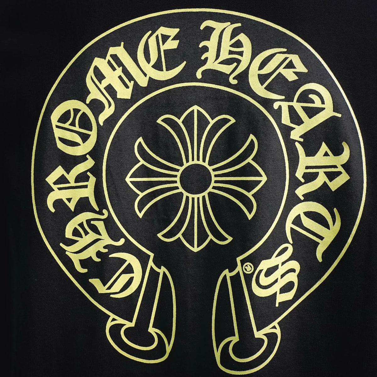 Close-up of black T-shirt back logo: circular gold design with central flower icon