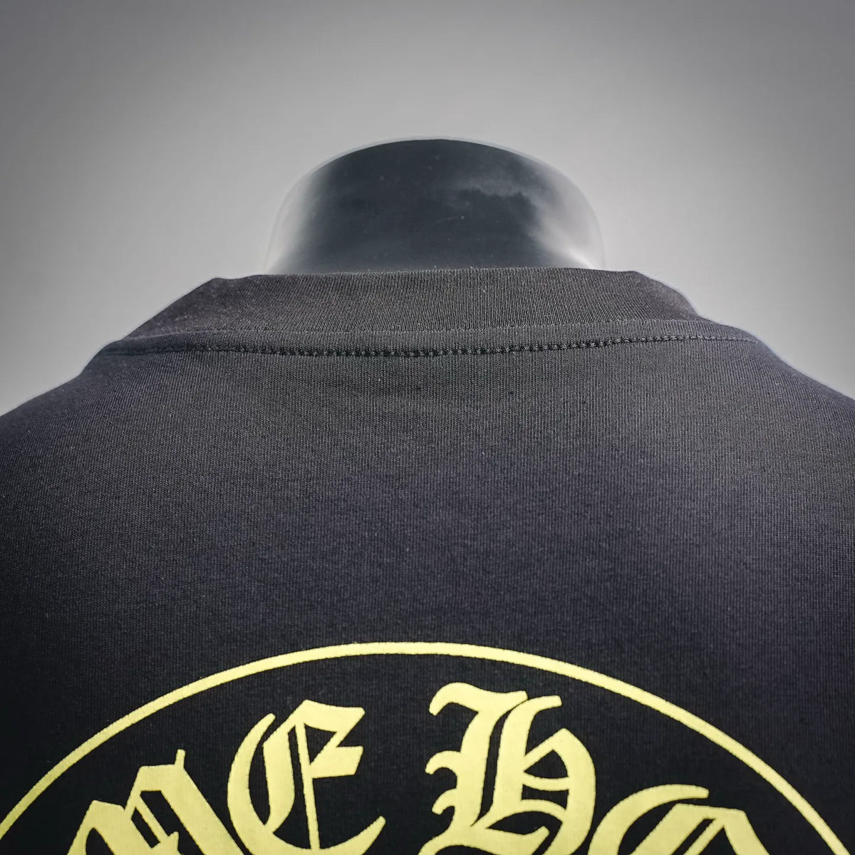 Back view of black T-shirt collar and upper shoulder with partial circular gold logo