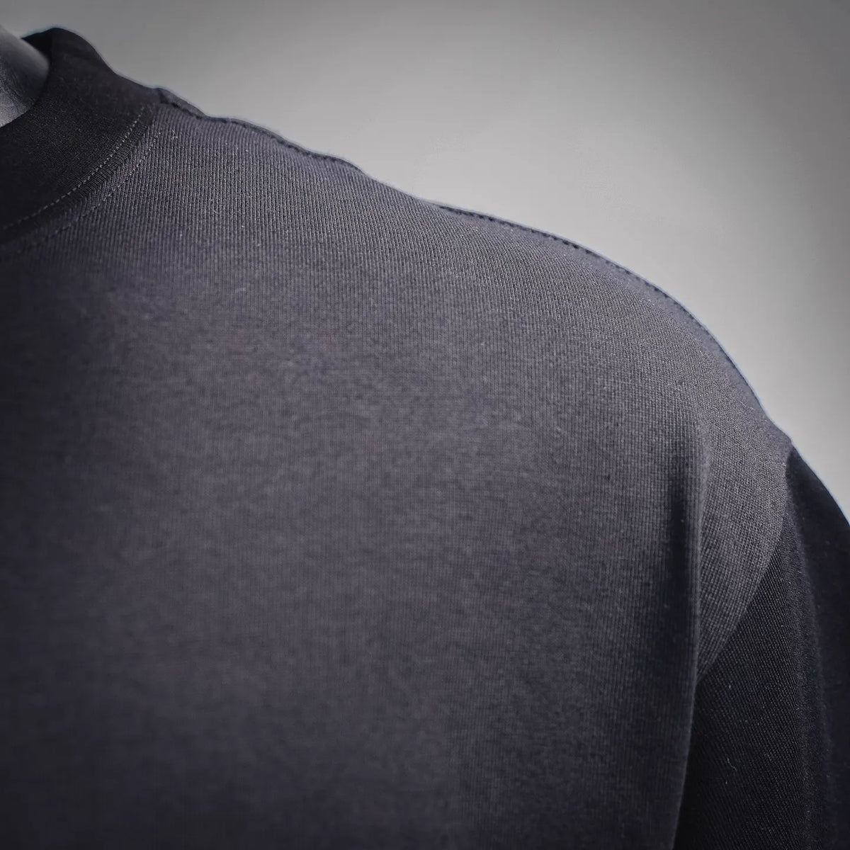 Black crew-neck T-shirt side panel with visible stitching seam and clean fabric surface