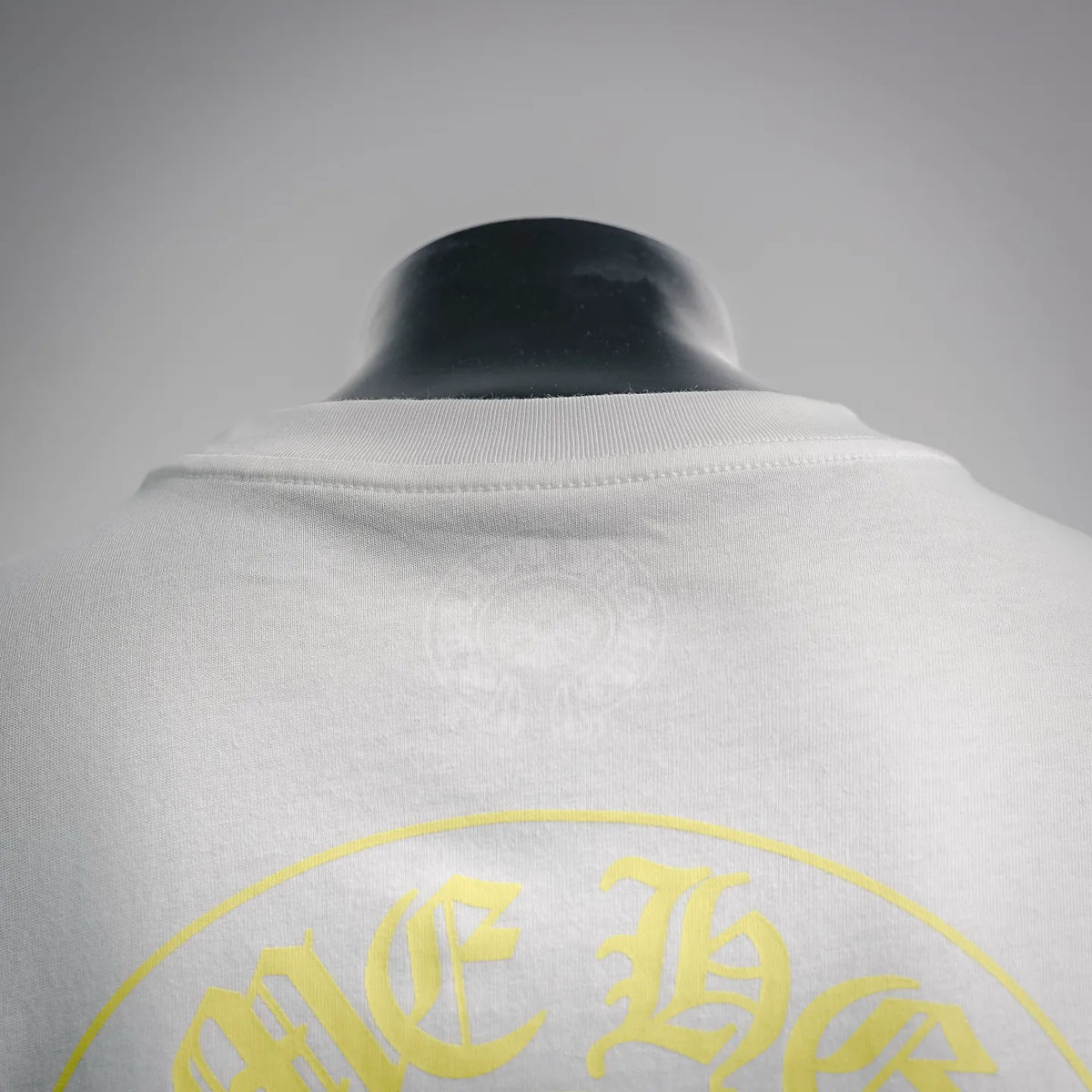 Back of white short-sleeve T-shirt with curved yellow logo graphic near collar