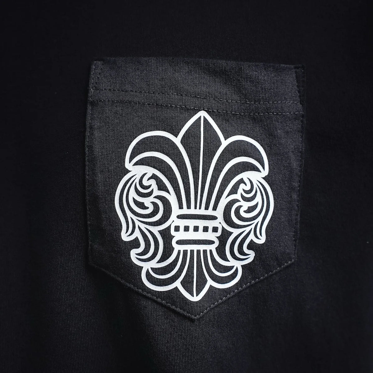 Black t-shirt chest pocket with white fleur-de-lis style emblem