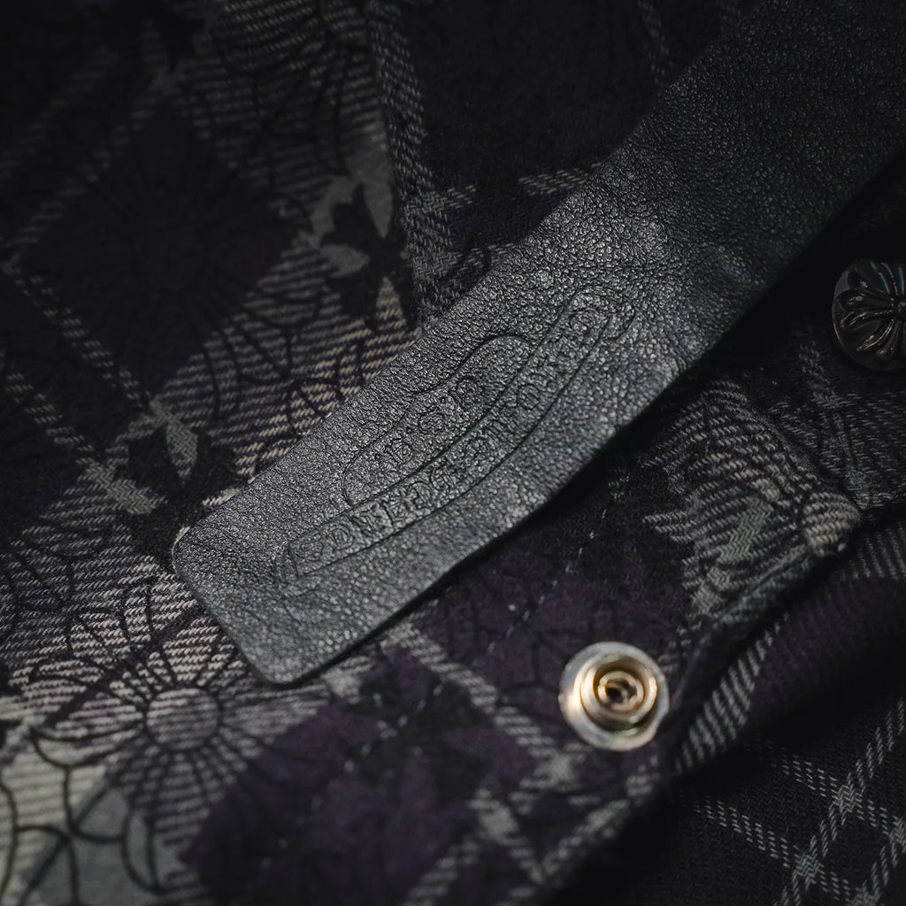 Close-up of dark plaid shirt fabric with floral stitching and metal snap button