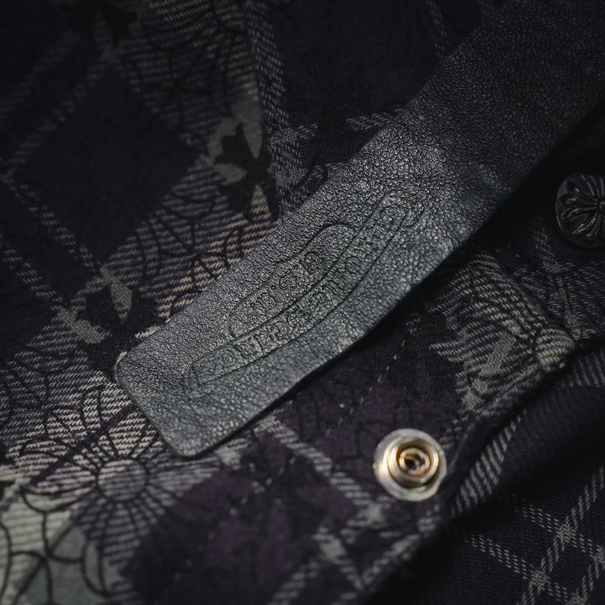 Close-up of dark plaid shirt fabric with floral stitching and metal snap button