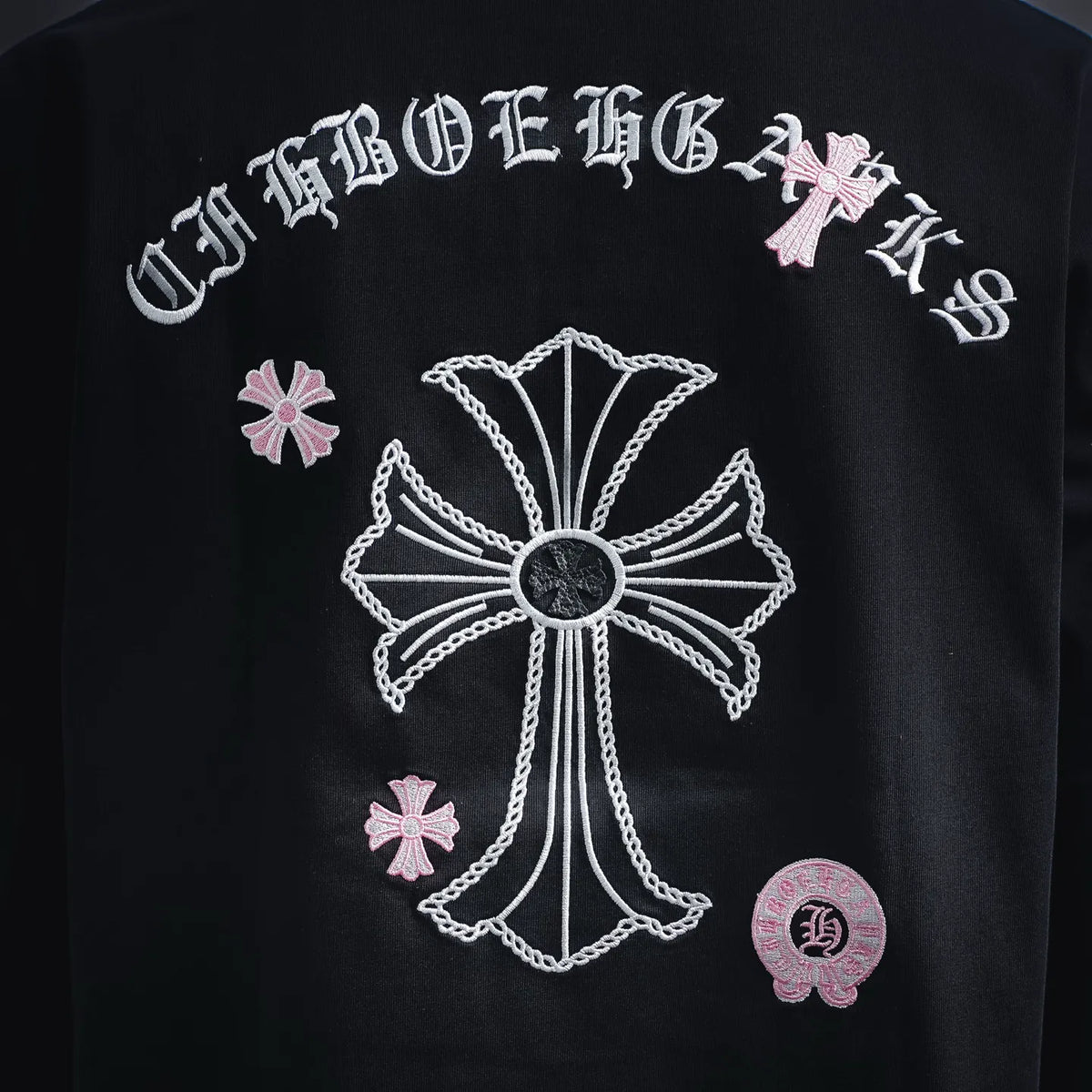 Dark T-shirt with detailed white cross emblem and pink flower accents on back.